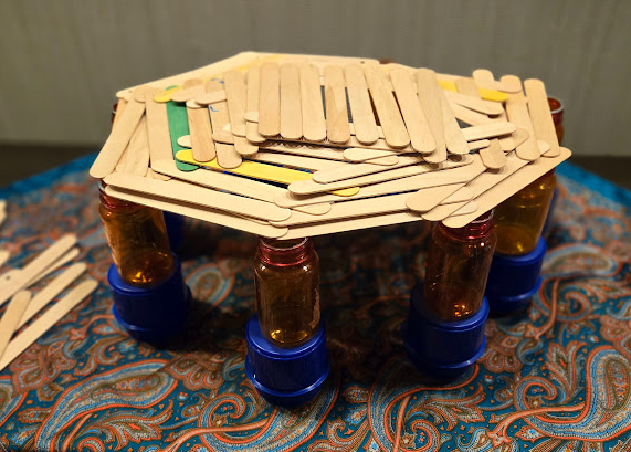 A structure built from popsicle sticks and small bottles using loose parts
