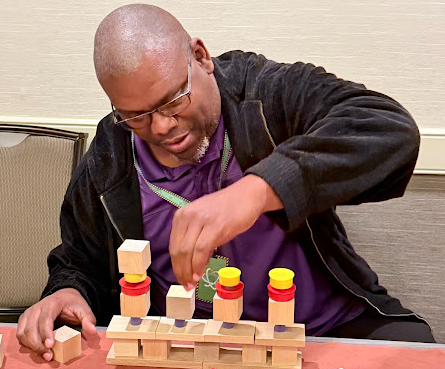 Adult educator carefully building a structure with wooden blocks and colorful loose parts materials