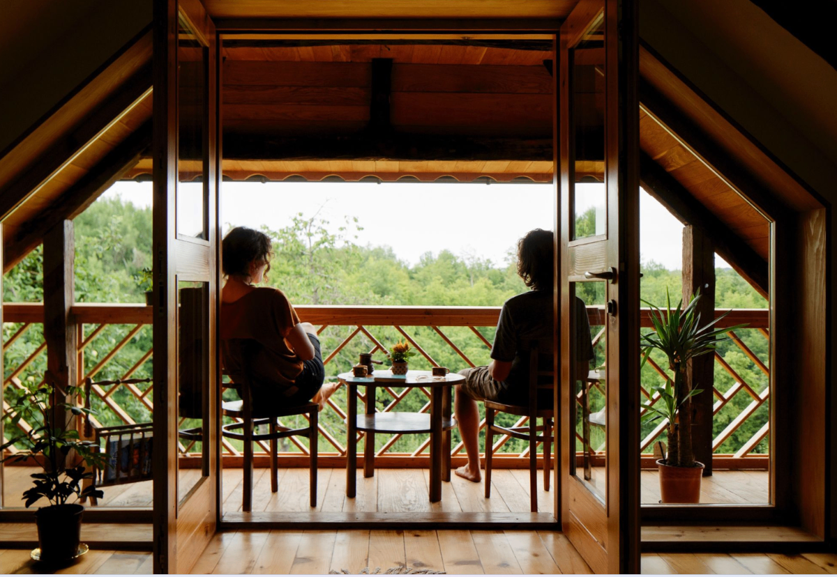 Two guests sitting on a wooden cabin balcony overlooking lush green forest