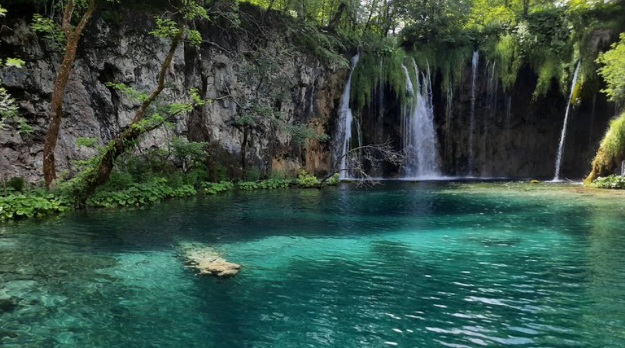 Crystal clear turquoise lake with cascading waterfalls and lush green forest at Plitvice Lakes