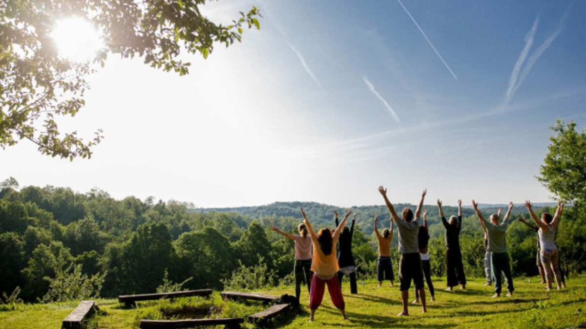 Group yoga session outdoors on a hilltop surrounded by lush green forest