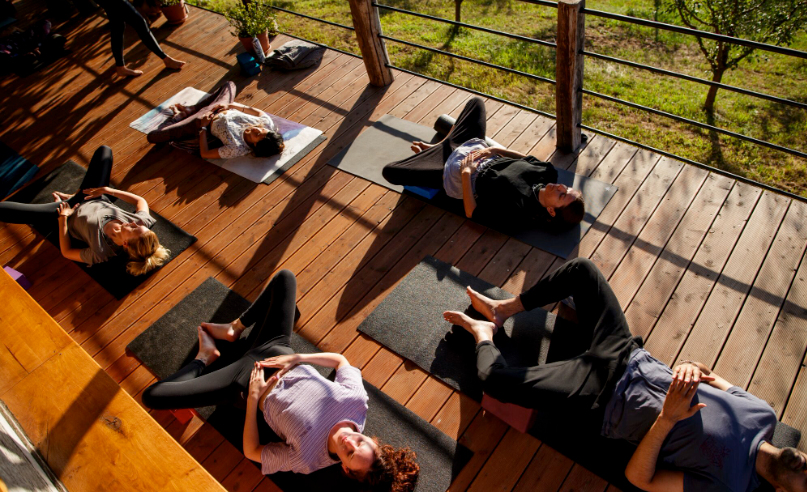 Aerial view of guests lying on yoga mats on a sunlit wooden deck surrounded by greenery