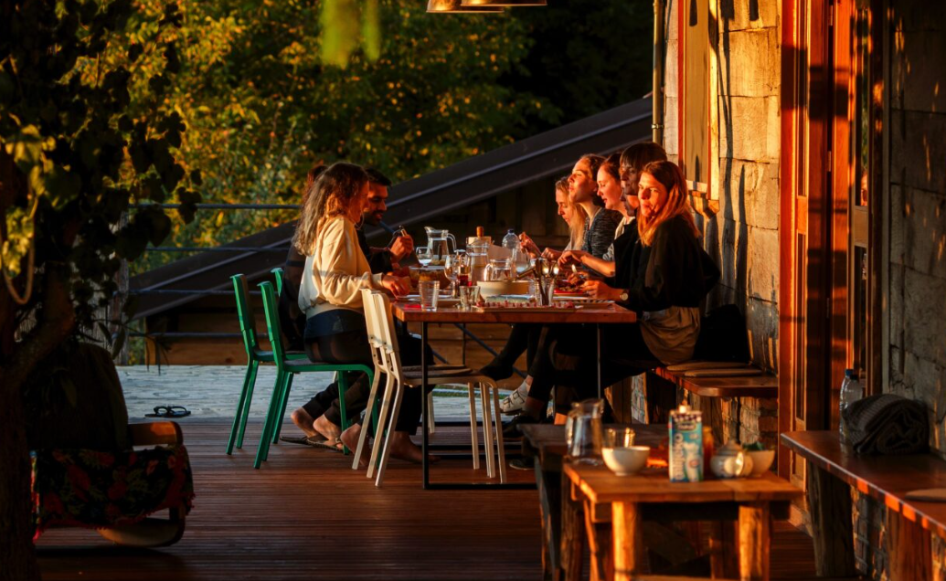 Guests dining together on a warm wooden terrace at golden hour surrounded by nature