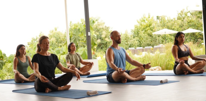 Group yoga meditation session in the light-filled studio with tropical garden views