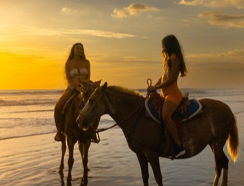 Horseback riding on the beach at golden sunset — two riders on the Pacific shoreline