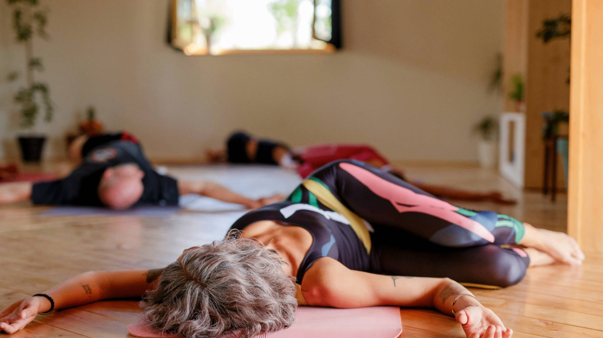 Yoga class participants in savasana relaxation pose on mats in a sunlit studio