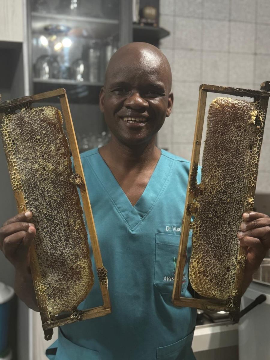 Dr Vusi at Arise & Shine holding fresh honeycomb frames in teal scrubs