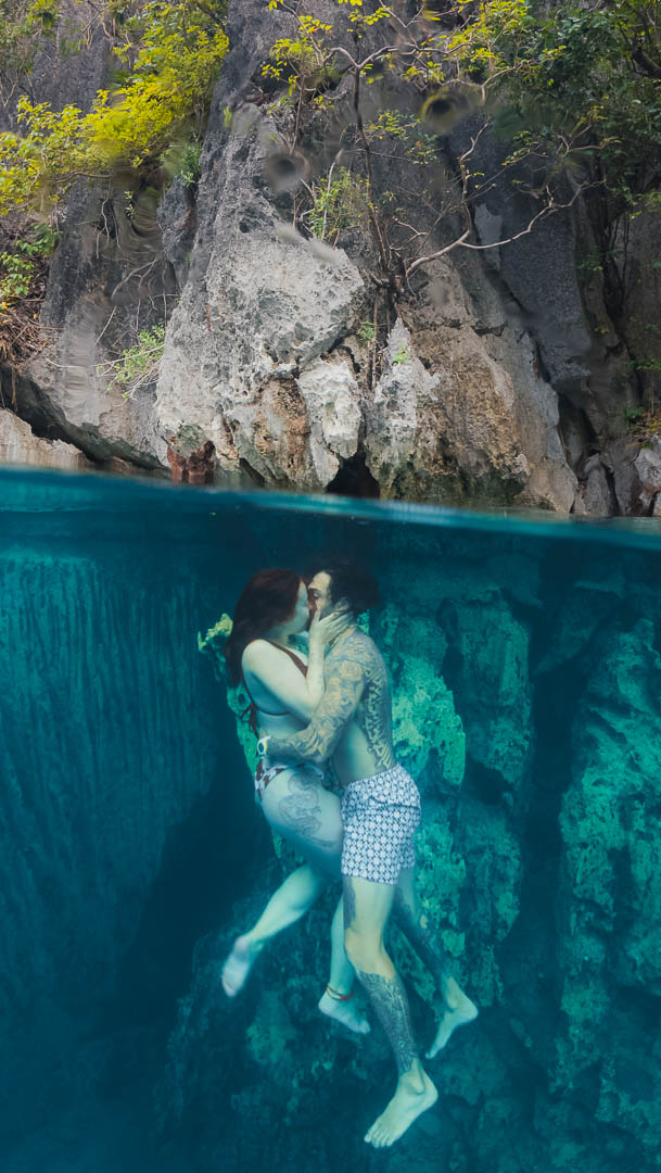 Couple kissing underwater at Barracuda Lake Coron Palawan Philippines split shot with limestone cliffs above