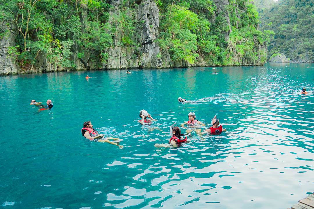 Tourists snorkeling and swimming in the crystal clear turquoise waters of Kayangan Lake Coron Palawan Philippines surrounded by dramatic limestone cliffs