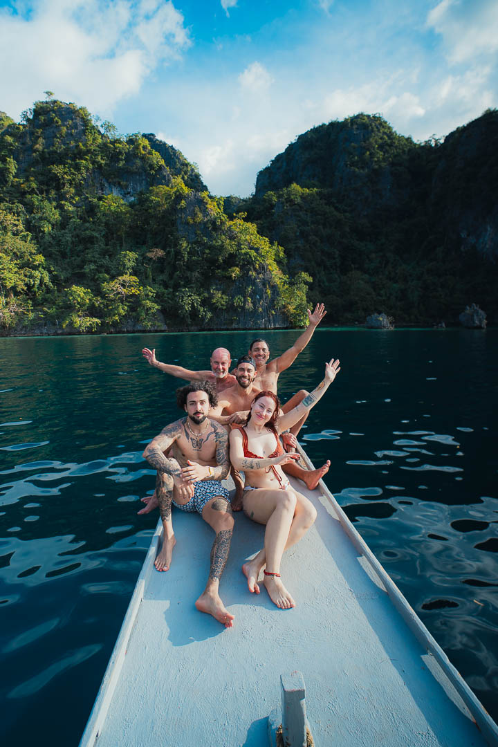 Happy group of tourists sitting on a traditional bangka boat in Coron Palawan Philippines surrounded by limestone cliffs and calm turquoise water
