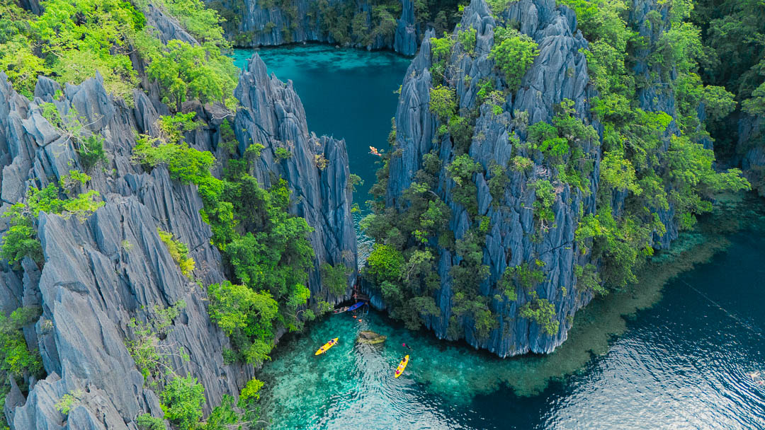 Aerial view of Coron Palawan Philippines dramatic limestone karst cliffs with kayakers on crystal clear turquoise lagoon