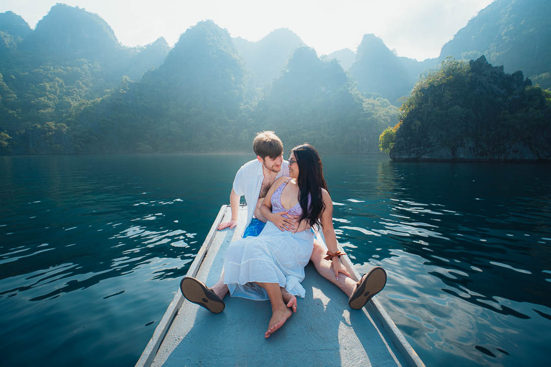Romantic couple sitting on the bow of a boat at Coron Palawan Philippines surrounded by misty limestone karst cliffs and calm turquoise water