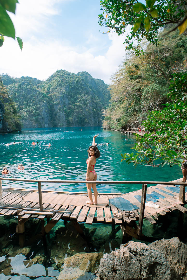 Woman posing on wooden boardwalk at Kayangan Lake Coron Palawan Philippines with turquoise water and lush limestone cliffs