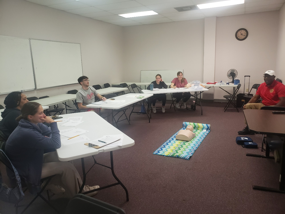 CPR classroom session with students seated at tables and CPR manikins on the floor at J. Jacobs Public Safety Tallahassee