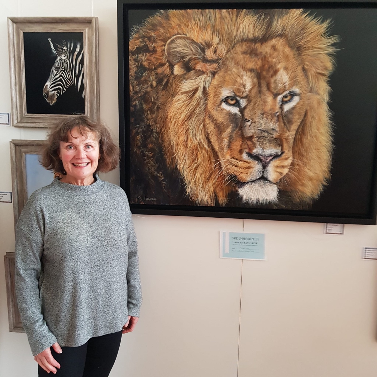 Fiona Champion standing beside her award-winning lion painting at The Canvas Club exhibition