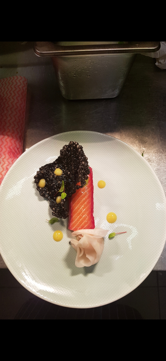 Cured salmon with black rice cracker and saffron aioli dots on a white plate