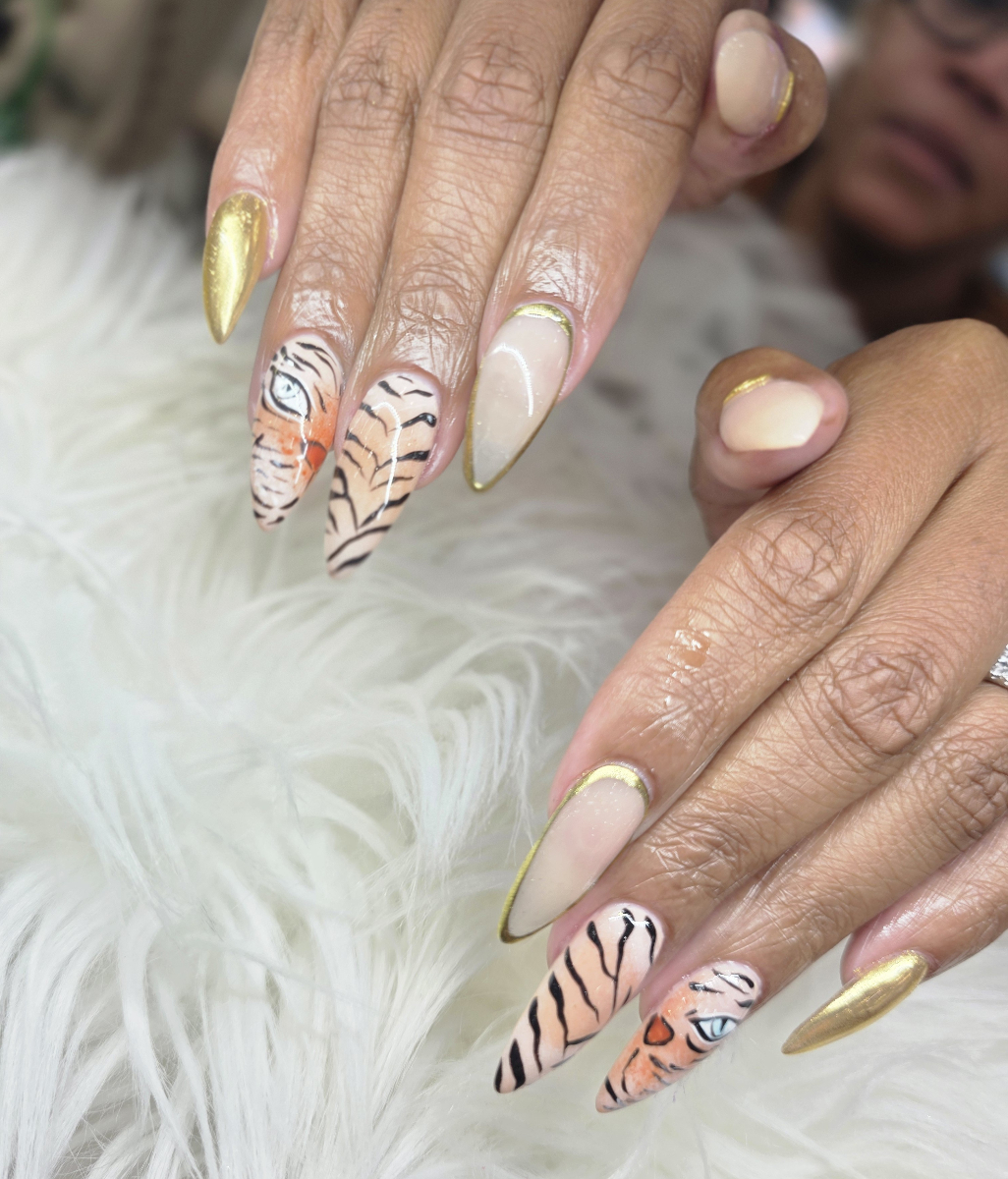 Detailed nail art featuring tiger print effects with golden details and elegant decorations showcasing advanced artistic techniques