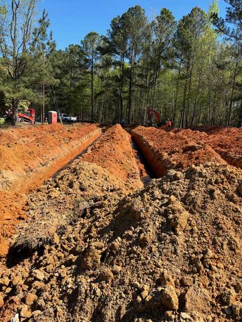 DLC Septic drainfield trench excavation showing deep parallel trenches dug in red clay soil in Rock Hill SC