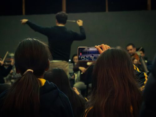 Estudiantes grabando con su celular al director de orquesta durante una experiencia Dentro de la Orquesta CNC