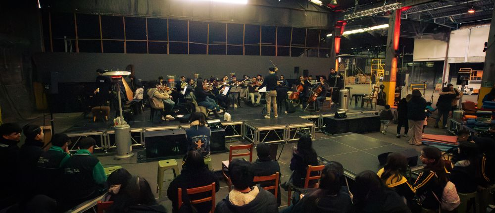 Ensayo de la orquesta CNC con público joven sentado frente al escenario en espacio industrial