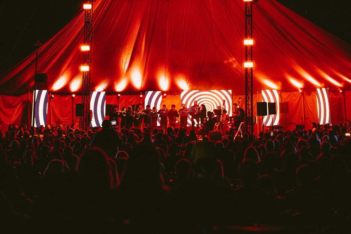 Orquesta CNC en carpa roja con luces y público — experiencia inmersiva