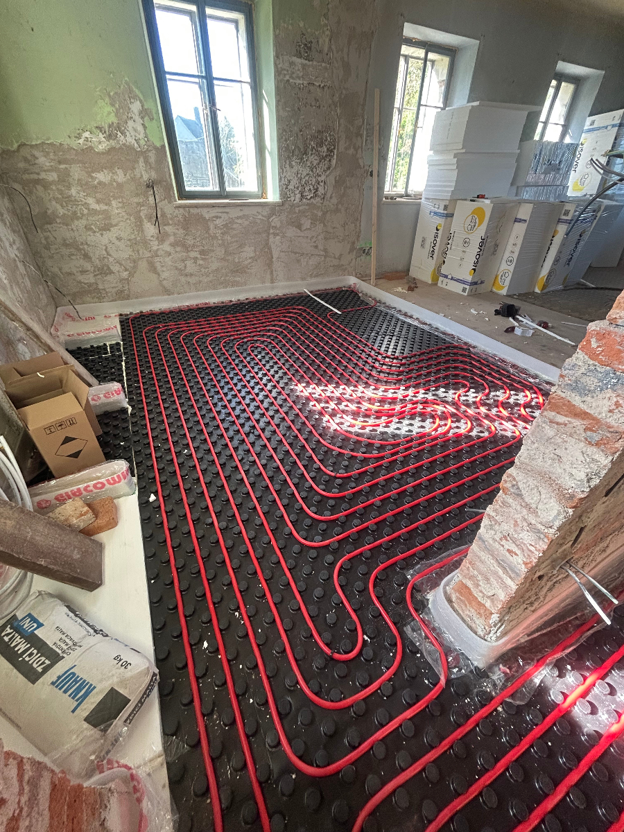 Instalace podlahového vytápění s červenými topnými trubkami v rozestavěném interiéru
