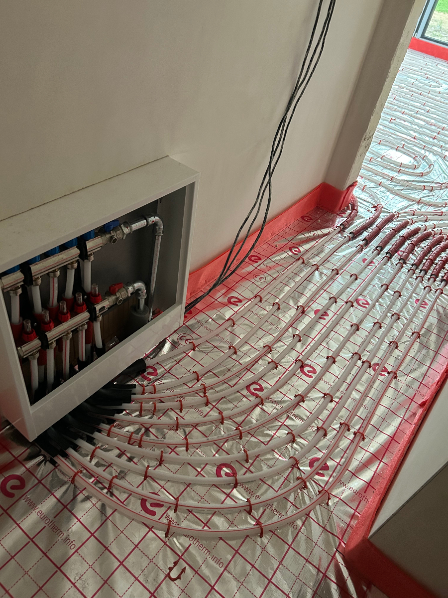 Instalace podlahového vytápění s rozdělovačem a červenými topnými trubkami v rodinném domě