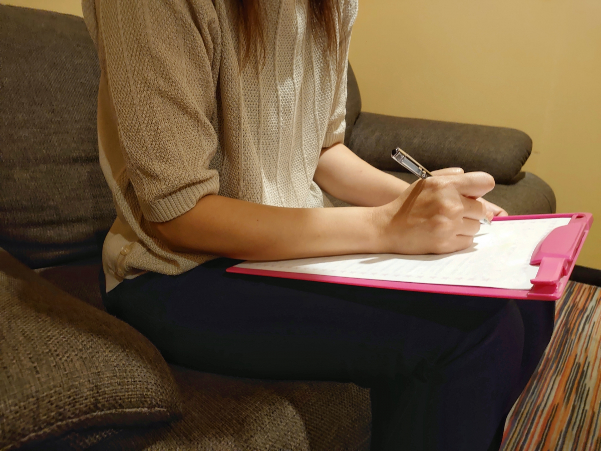 木の受付カウンターで問診票を書く女性