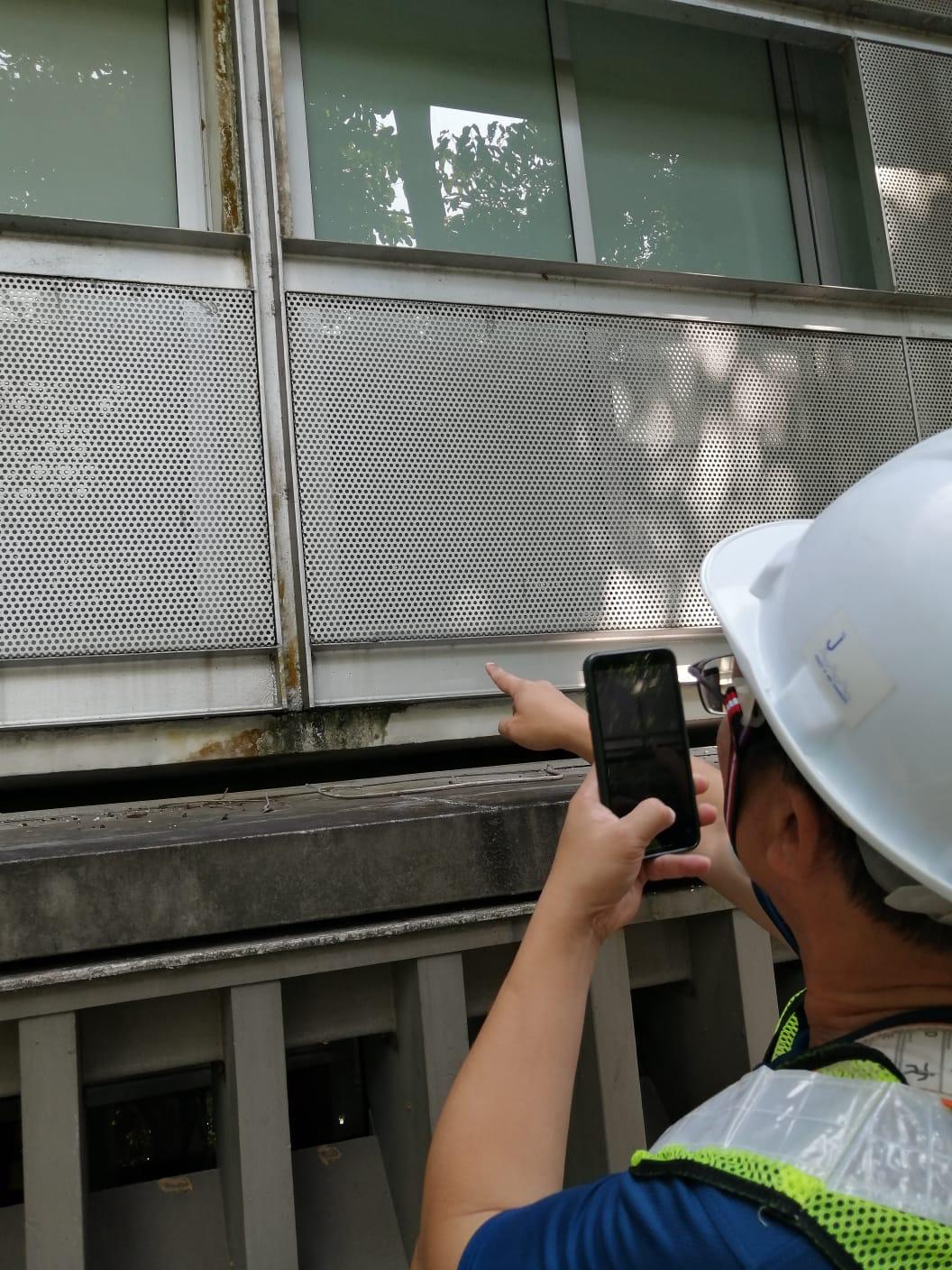 Close-up facade inspector examining external wall cladding and sealant joints on a Singapore commercial building