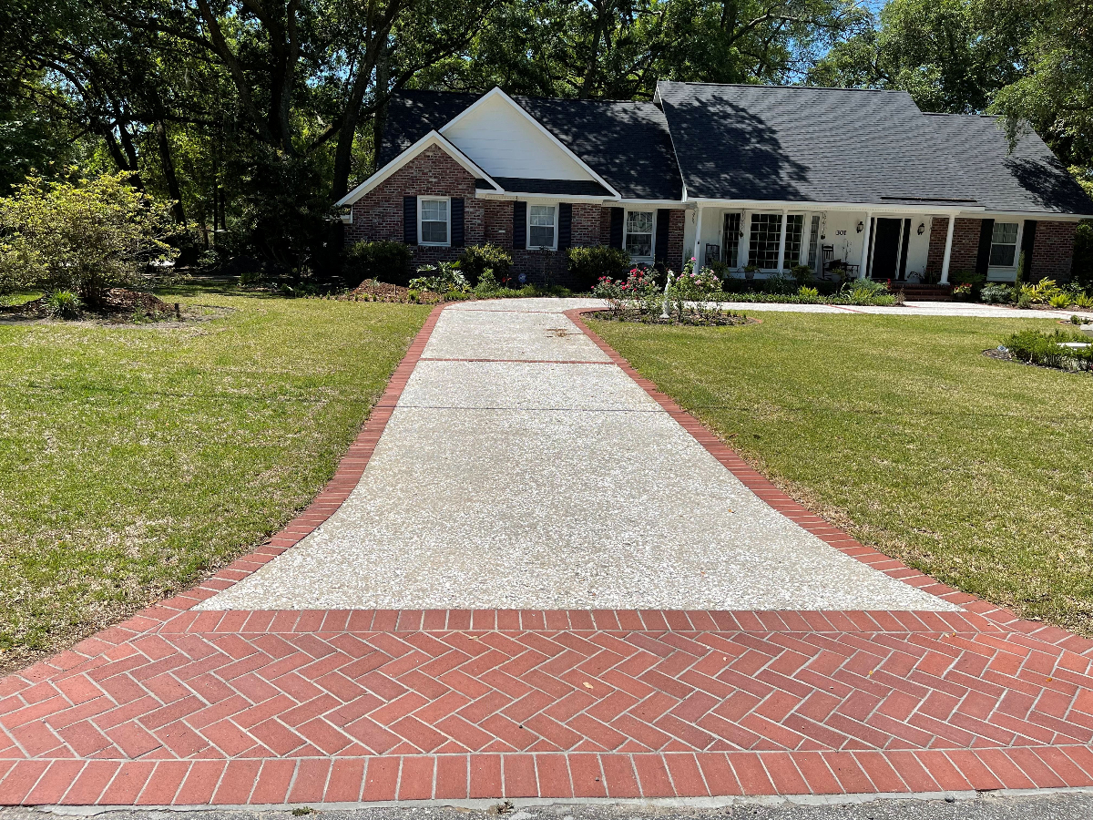 Professional concrete apron installation Charleston SC showing smooth transition from driveway to street with red brick border, exposed aggregate walkway, and expert craftsmanship for residential property