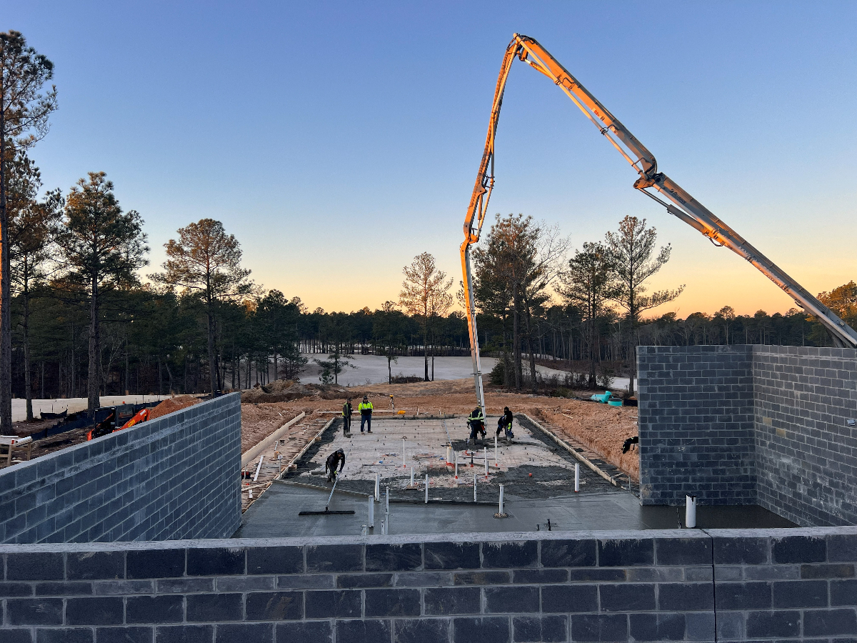 Concrete Foundation Construction - Charleston SC Professional concrete foundation construction showing slab-on-grade installation with 8-10 inch thickness, 4000 PSI concrete, #4 steel rebar grid reinforcement, 6 mil vapor barrier, compacted gravel base, wooden formwork, concrete pouring and leveling, smooth trowel finish, control joint cutting, proper drainage slope, and expert foundation contractors for residential and commercial buildings in Charleston SC Lowcountry