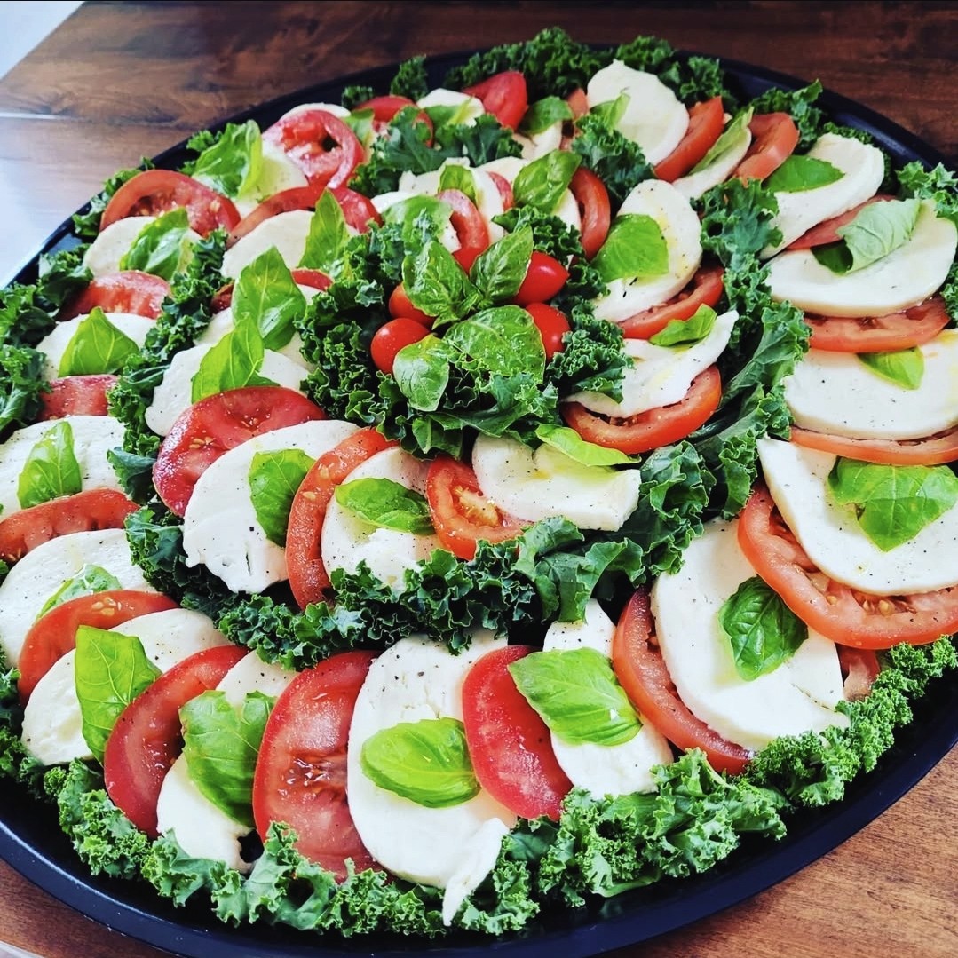 Fresh caprese platter with sliced mozzarella, tomatoes, basil and kale from Palleschi Pizza catering